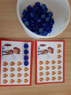 two blue and orange buttons next to a white bowl filled with blue plastic balls on top of a wooden table