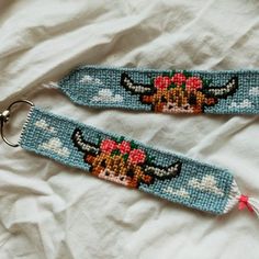 two cross stitch keychains are laying on a white sheet and one has a red flower in it