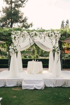 an outdoor wedding setup with white flowers and draping on the back drop cloths