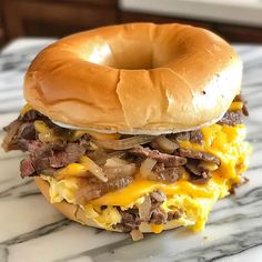 a sandwich with meat, cheese and onions on a bagel bun sitting on a marble surface