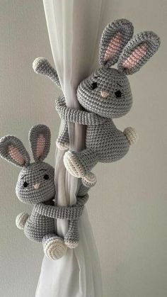 two crocheted rabbits are hanging from the side of a white curtain with their ears wrapped around them