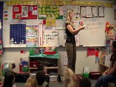 a woman standing in front of a whiteboard with writing on it and people sitting around