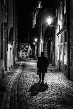 a man is walking down an alley way at night with his cane in the dark