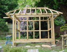 a wooden structure in the middle of a yard with purple flowers growing on it's side