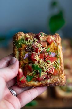 a person holding up a piece of bread with toppings on it