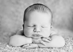 a black and white photo of a baby laying on its back with his eyes closed