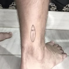 a man's foot with a small surfboard tattoo on his left side leg