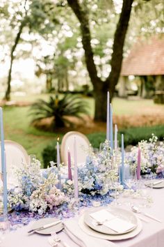 the table is set with blue and white flowers, candles, and napkins on it