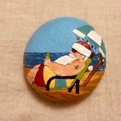 a painted rock with a man sitting in a chair on the beach and holding a bottle