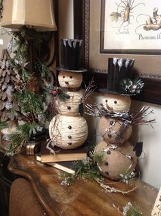 three snowmen sitting on top of a wooden table next to a lamp and christmas tree