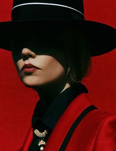 a woman wearing a red coat and black hat with pearls on her necklace, standing in front of a red background