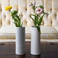 two vases with flowers in them sitting on a table next to a white couch