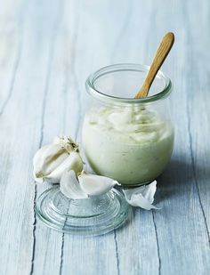 a glass jar filled with cream next to a wooden spoon and garlic florets