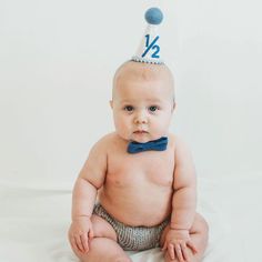 a baby sitting on the floor wearing a blue bow tie and a birthday cake hat