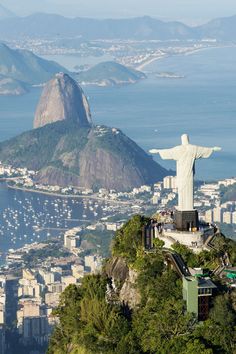 a statue on top of a hill overlooking the city and water with mountains in the background