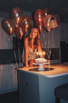 a woman sitting in front of a cake with lit candles on it and balloons behind her