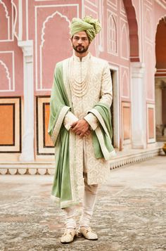 a man in a green turban standing on the ground with his hands behind his back