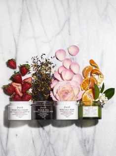 three different types of body scrubs with flowers and fruit on the side, including strawberries