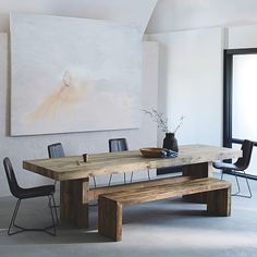 a wooden table sitting in front of a painting on the wall next to two black chairs