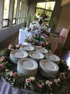 many plates are arranged on a table with flowers and greenery in the centerpiece