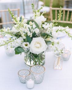 a vase filled with white flowers sitting on top of a table next to two candles