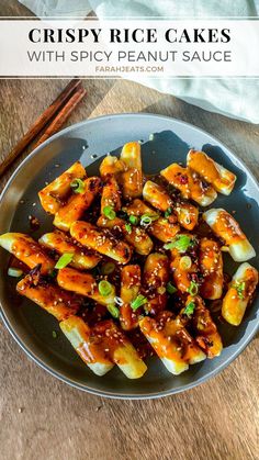 Plated crispy tteokbokki rice cakes with spicy peanut sauce, garnished with green onions and sesame seeds. On the side is a pair of wooden chopsticks and a white kitchen towel. Tteokbokki Rice Cakes, Crispy Rice Cakes, Korean Side Dishes, Spicy Peanut Sauce, Crispy Rice, Peanut Sauce