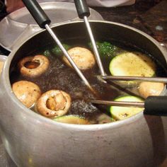 a pot full of food with tongs sticking out of the top and vegetables cooking in it