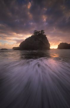 the sun is setting over an island in the ocean with waves coming up on it