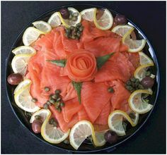 a platter with salmon, lemons and olives on the side as well as an orange flower