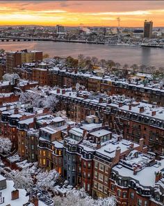 an aerial view of snow covered buildings and the water in the background at sunset or dawn