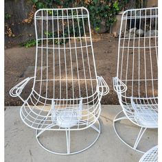 two white wire chairs sitting next to each other on a sidewalk in front of a house