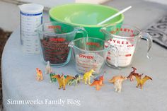 plastic toy dinosaurs and measuring cups on a cement table with an empty cup next to them