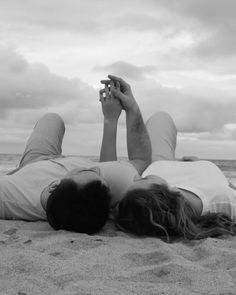 a man laying on the beach with his feet up in the air while holding a cell phone