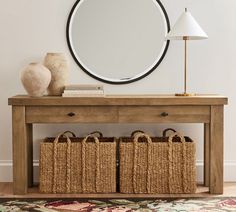 a wooden table with baskets under a round mirror on top of it next to a lamp