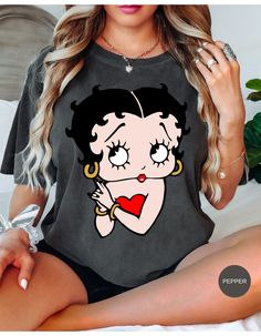 Step back in time with our Vintage Betty Boop Charm Tee! Featuring the iconic cartoon sweetheart in her classic pose, this t-shirt is perfect for adding a touch of retro flair to your wardrobe. Made from soft, high-quality cotton, it offers a comfortable fit for everyday wear. Whether you're a long-time fan or just love vintage vibes, this tee will have you booping with style! Retro Short Sleeve Top With Cartoon Print, Retro Crew Neck Top With Heart Graphic, Retro Black Top With Cartoon Print, Vintage Black T-shirt With Cartoon Print, Vintage Black Top With Cartoon Print, Vintage Betty Boop, Iconic Cartoon, Step Back, Love Vintage