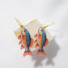 two fish shaped earrings sitting on top of a piece of white paper next to each other