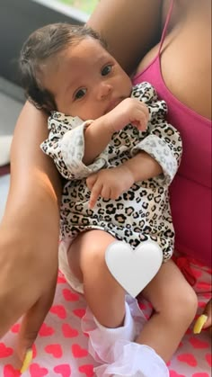 a woman holding a baby in her arms on top of a blanket with hearts all over it