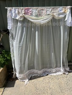 a white curtain with lace hanging from it's side on the ground next to a potted plant