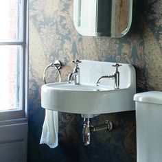 a white sink sitting next to a toilet in a bathroom under a mirror and a window