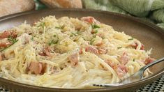 a plate of pasta with ham and parmesan cheese on the table next to bread