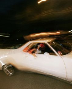 a white car driving down a street next to a person in the driver's seat