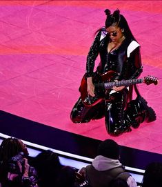 a woman in black and white outfit holding a guitar on stage with people around her