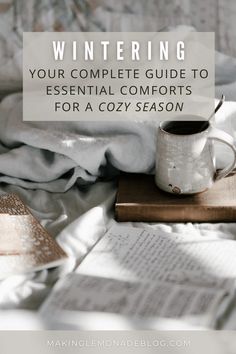 an open book and cup on top of a bed with the title wintering your complete guide to essential comforts for a cozy season