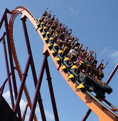 an amusement park ride with people riding on the roller coasters in front of a blue sky