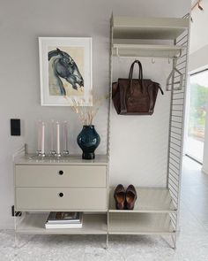 a white shelf with shoes and purses on it next to a wall mounted art