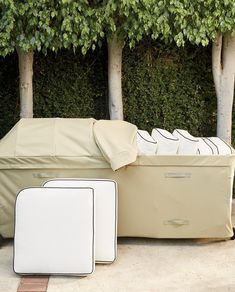 an outdoor covered bench and ottoman in front of some trees with white cushions on it