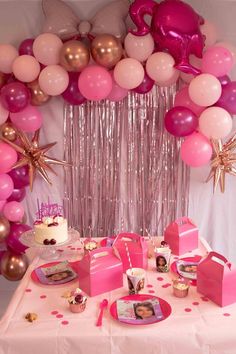 a table topped with lots of pink and gold balloons next to a cake on a plate