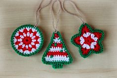 crocheted ornaments are hanging from strings on a wooden surface, decorated with red and white flowers