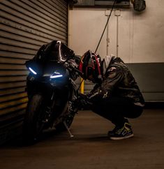 a man kneeling down next to a motorcycle in front of a garage door with the lights on