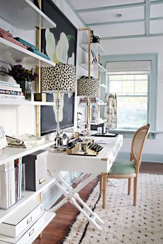 a white desk sitting in front of a window next to a chair and bookshelf